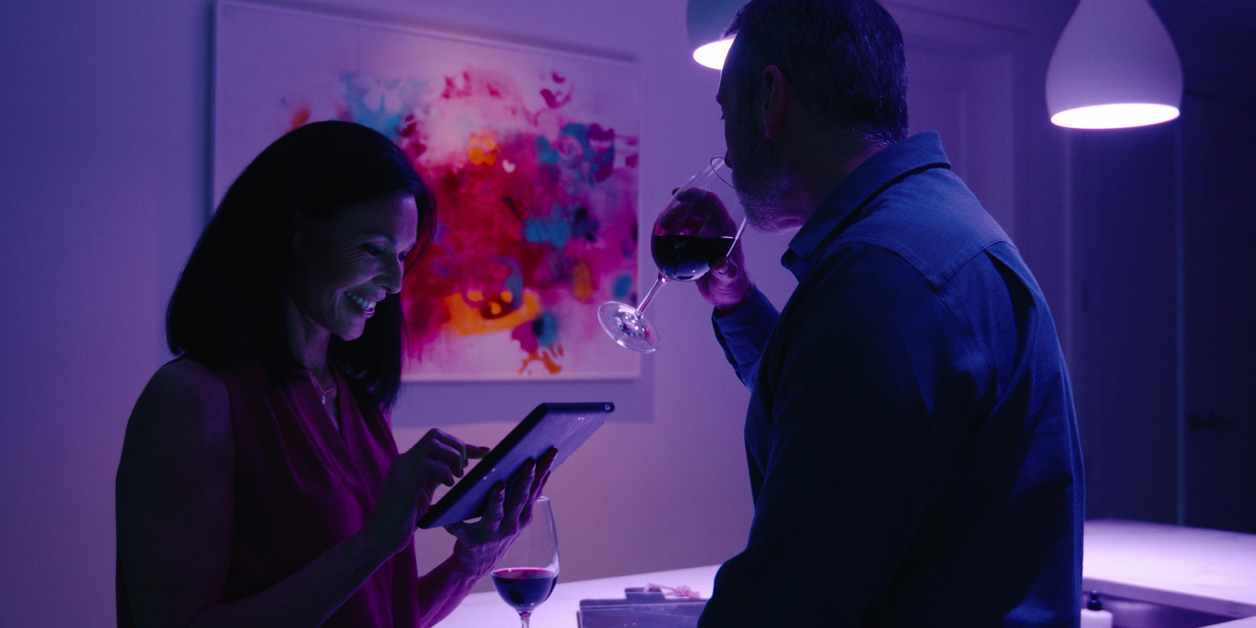 Couple enjoying wine while using tablet in purple-lit room