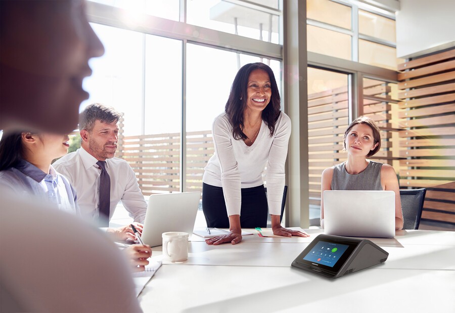 A woman is smiling at her team seated around a conference table during a meeting.