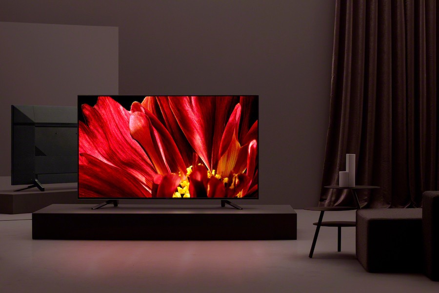 Sony 4K TV with red flower display sitting on a pedestal box in a darkened room.