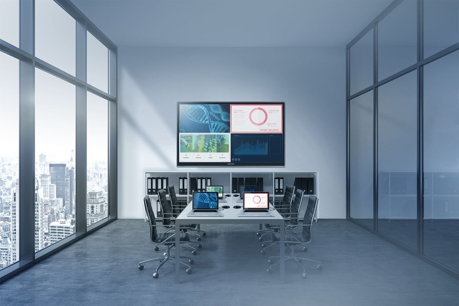 A conference room with a large display and four laptops on a table.