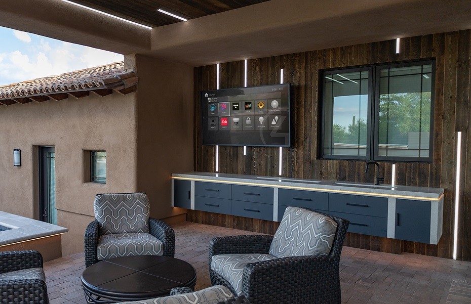  spacious outdoor patio featuring a wall-mounted TV showing the Control4 smart home interface above a sleek blue cabinetry, with stylish outdoor furniture.