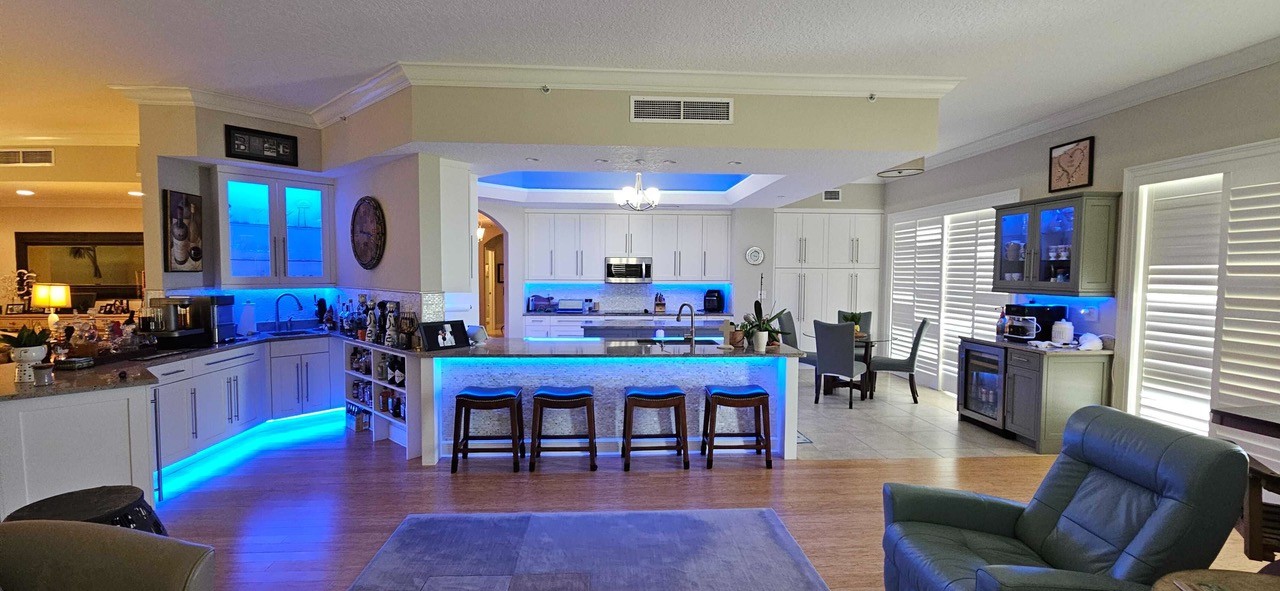 A luxury kitchen area with custom blue lighting in the ceiling, island, and cabinets.