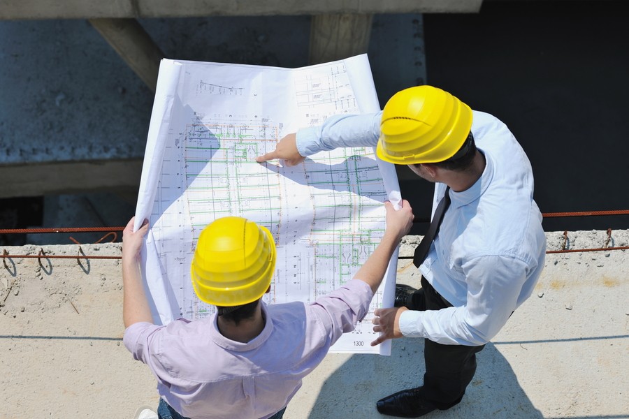Two construction professionals in yellow hard hats reviewing building plans at a construction site.