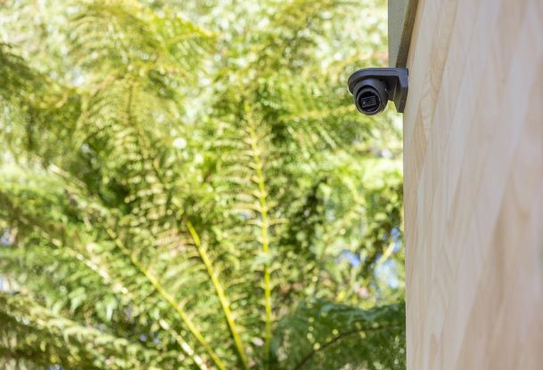 Security camera mounted on exterior wall with trees in background